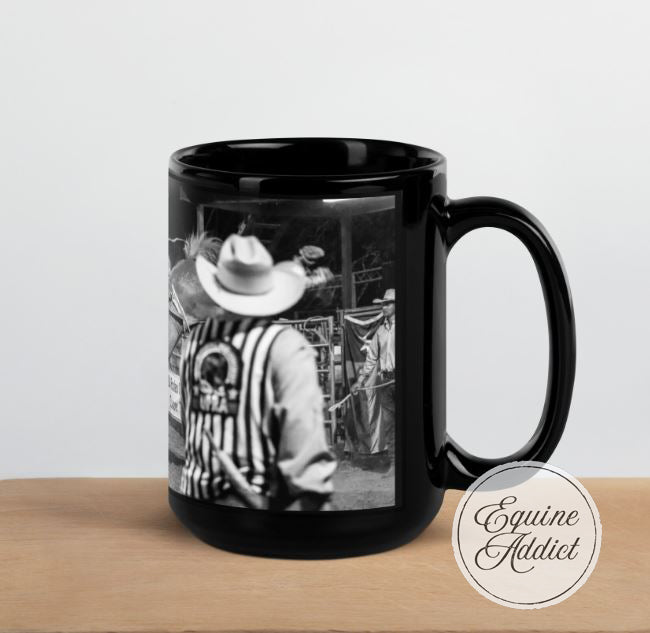 black ceramic mug featuring a rodeo scene, looking over the judges shoulder watching a cowboy ride a bucking horse