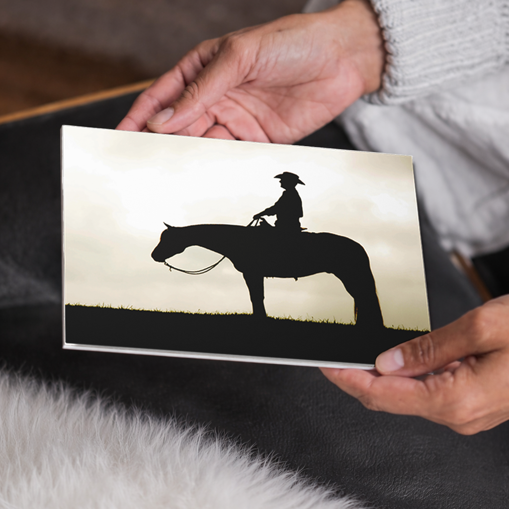 Person holding a photo with a silhouette of a cowboy on a horse